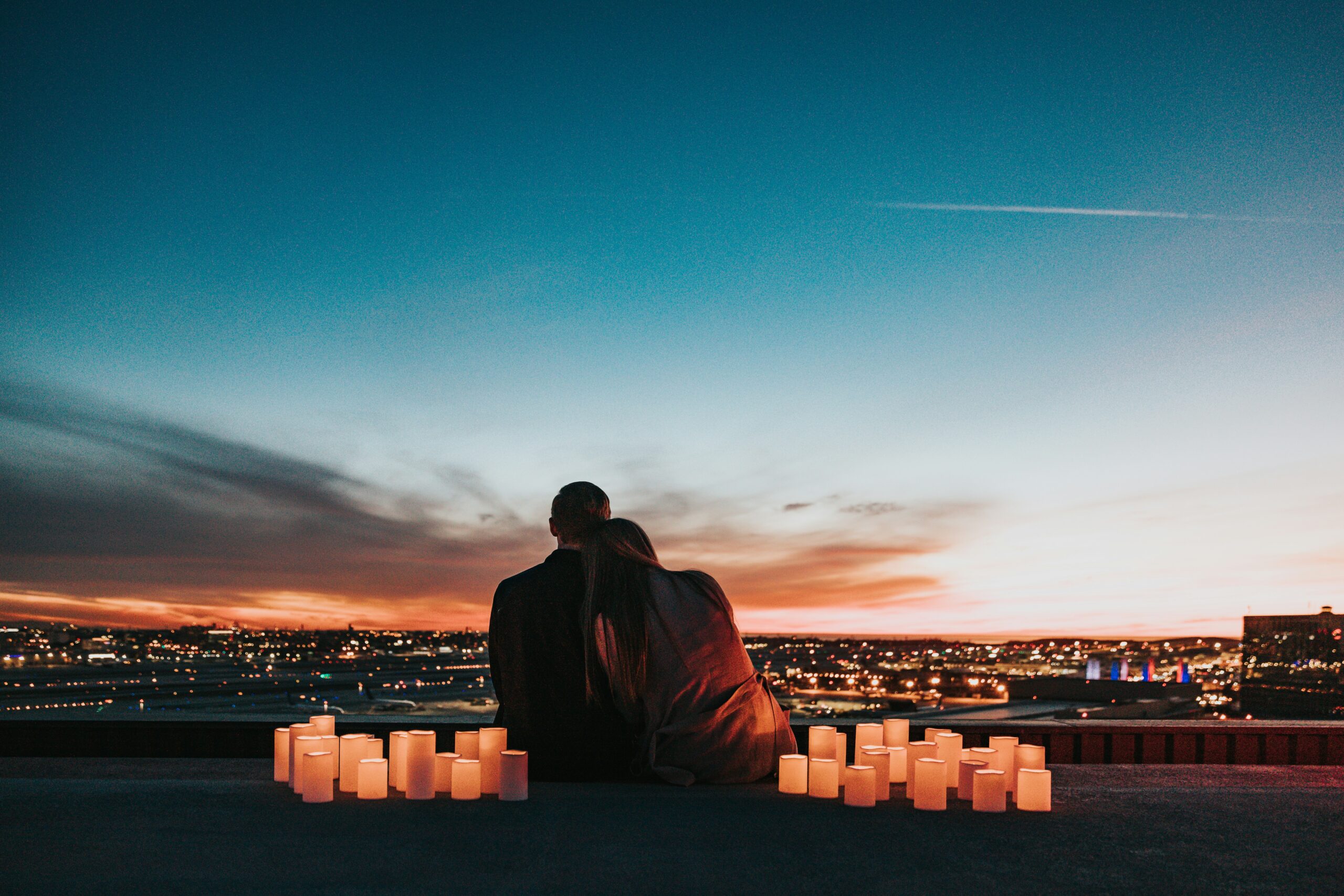 Things to Do in Raleigh: Couple leaning on each other overlooking the Raleigh city landscape with candles around them on a romantic evening.